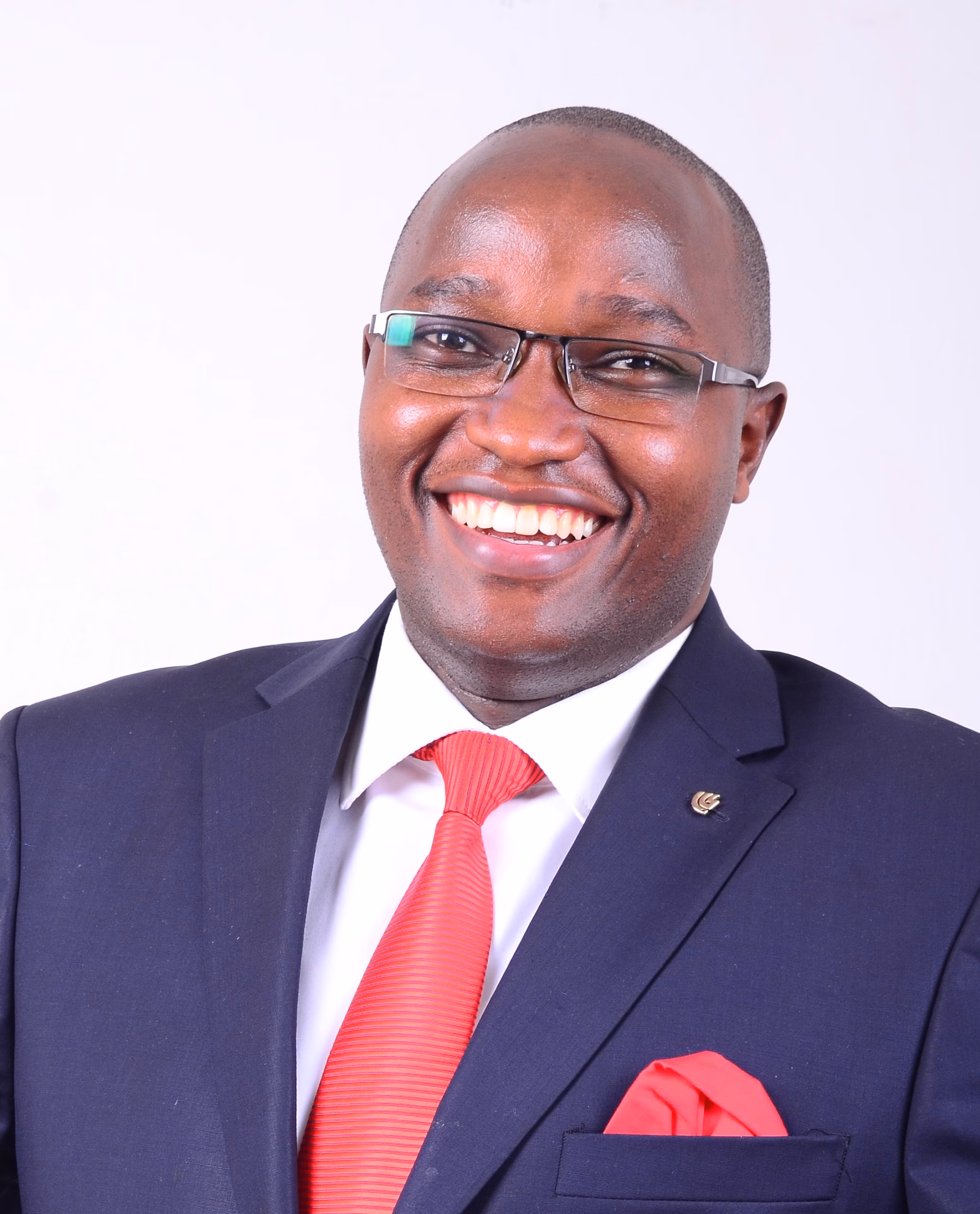 Portrait of Mukurweini MP John Kaguchia wearing glasses, navy suit, and red tie